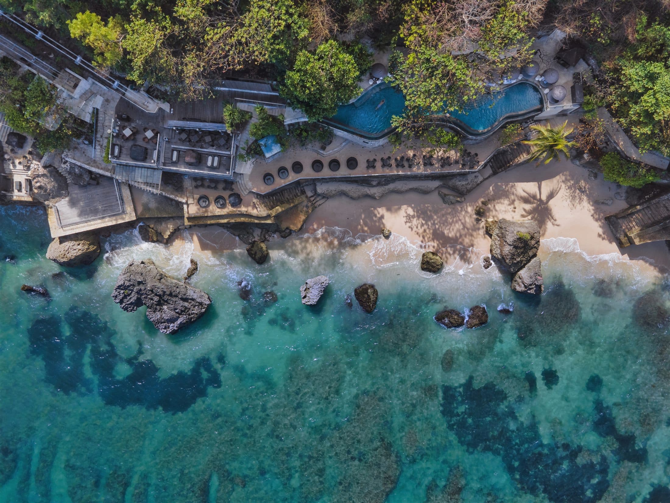 Aerial view of a coastal cafe terrace beside a turquoise shoreline.