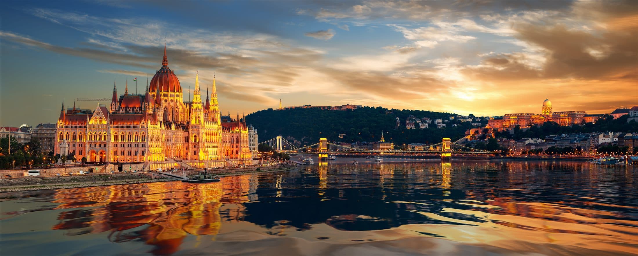 Wide evening view of Budapest with illuminated historic buildings along the river.