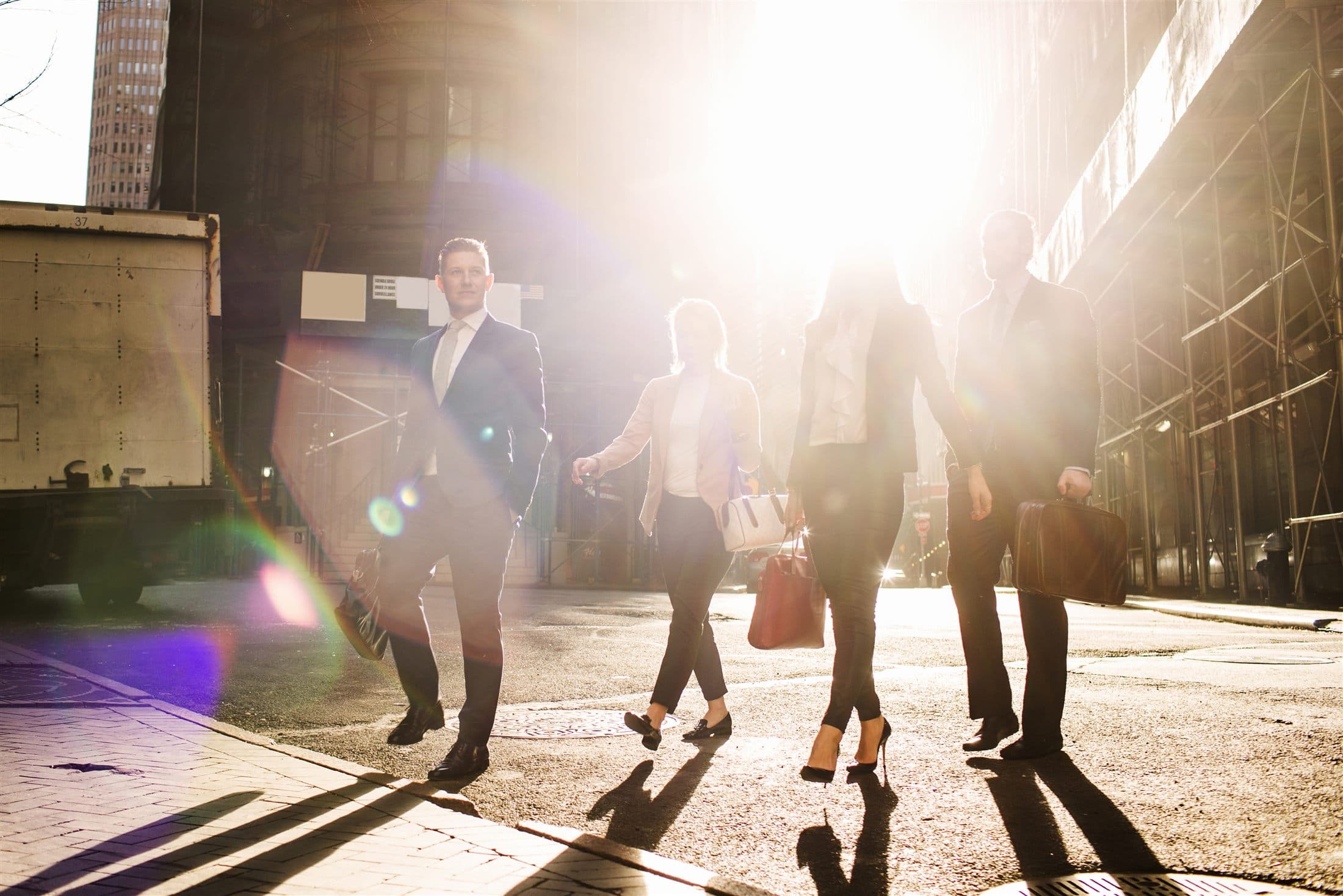 Business professionals walking past a classic stone building in warm daylight.